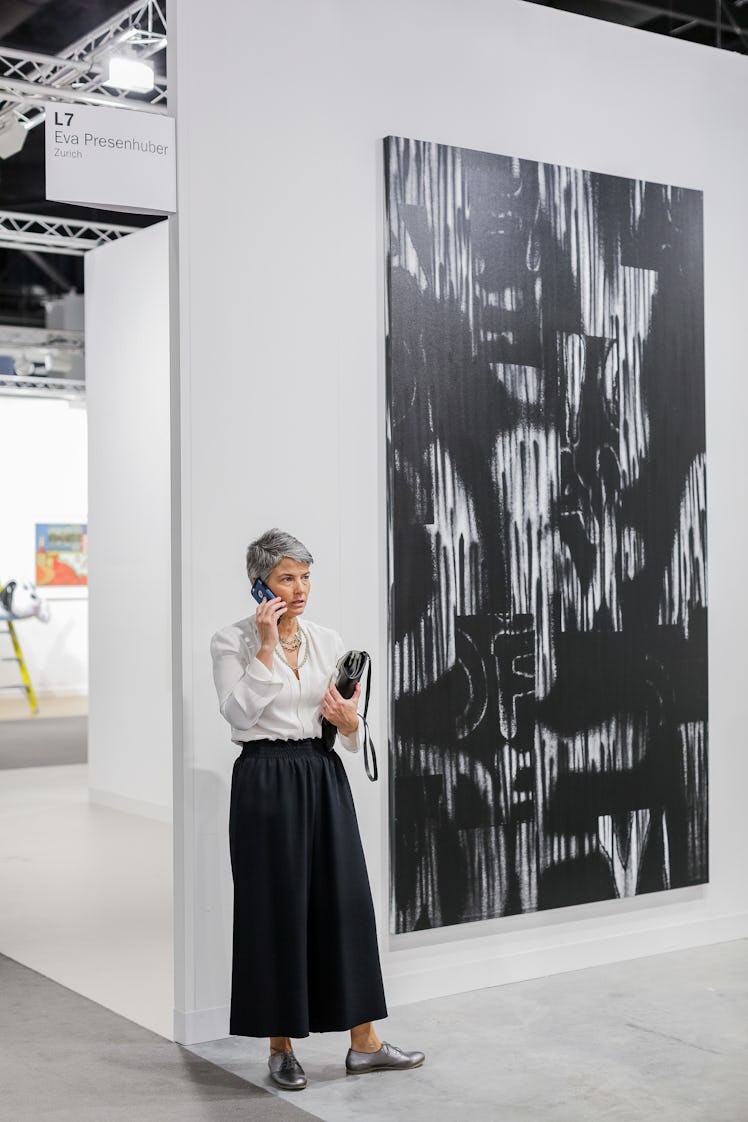 A woman talking on her phone while standing next to a painting at Art Basel Miami Beach 2016.
