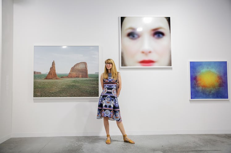 A woman in a patterned dress posing beside the paintings at Art Basel Miami Beach 2016.