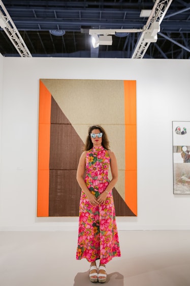 A woman in a pink floral maxi dress posing in front of the artwork at Art Basel Miami Beach 2016.