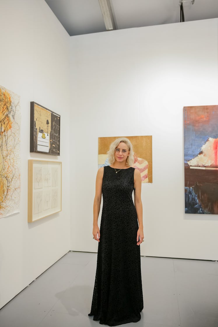 A woman in a long black dress posing beside paintings at Art Basel Miami Beach 2016.