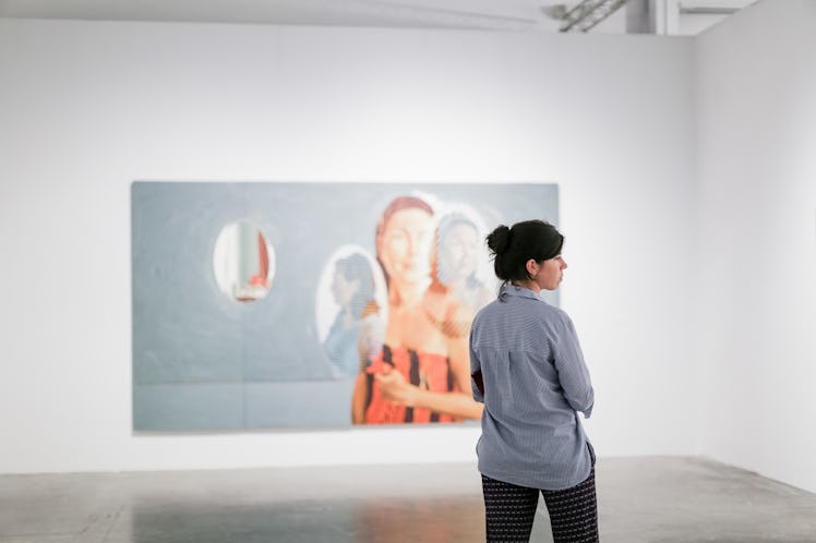 A woman wearing blue shirt and stripy pants with a painting in front of her at Art Basel Miami Beach...