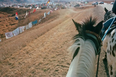 A person riding a horse taking a photo of a scene from a protest at Standing Rock