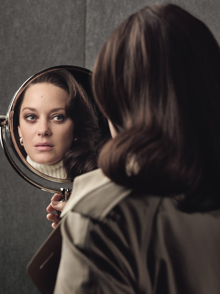 Marion Cotillard holding a mirror a mirror and looking into it while wearing a white sweater