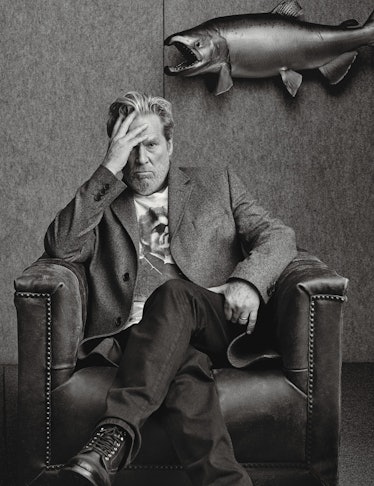 A portrait of Jeff Bridges sitting in an armchair with his hand on his forehead in black and white