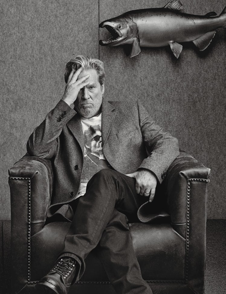 A portrait of Jeff Bridges sitting in an armchair with his hand on his forehead in black and white