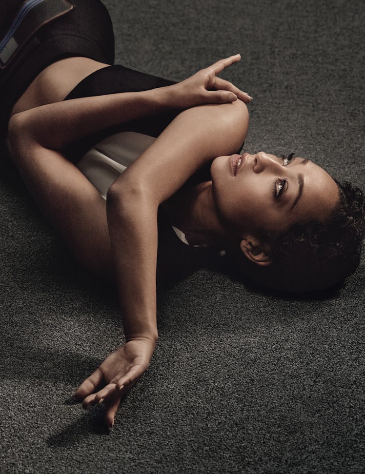Ruth Negga in a black top and pants lying on her back with her arms crossed while looking up