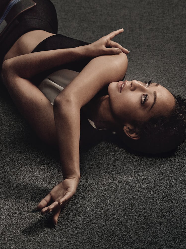 Ruth Negga lying and posing in a black top and black leggins