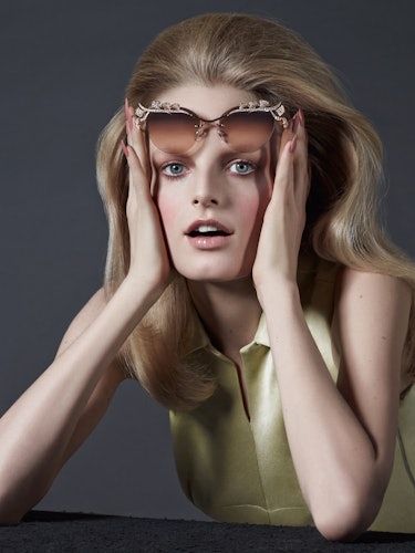 A blonde model with blue eyes, holding her sunglasses on her forehead 