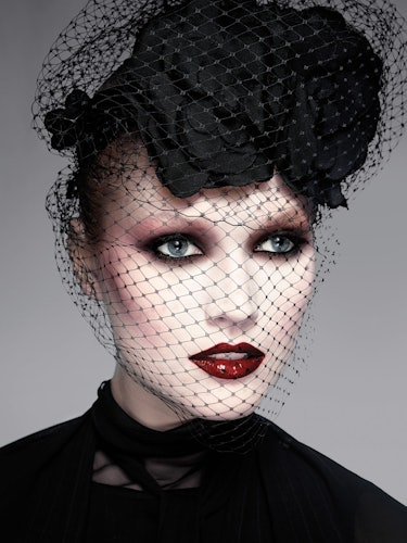 A model wearing a black floral headpiece with lace covering her face, a smoky eye and red lipstick 