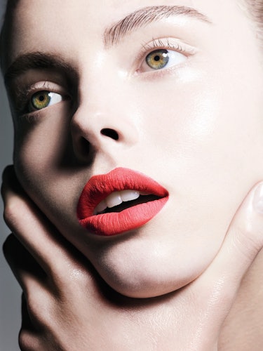 A model with pale skin and red lipstick holding her face 