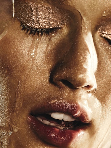 A closeup of a model with water dripping down her face and her golden eyeshadow staying in tact 