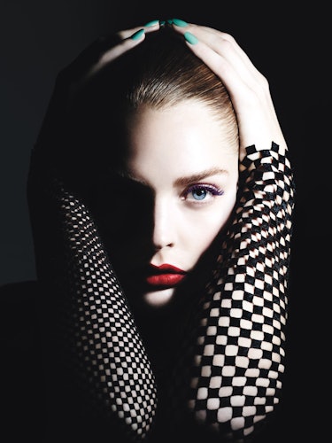 A model with blue eyes, long black eyelashes and red lipstick holding her face between her arms 