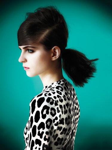 A brunette model with a low ponytail and deep side part, smoky eye and in a leopard-print blouse 