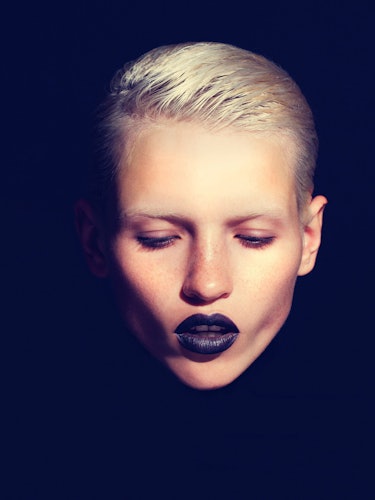 A blonde model with short hair and black lipstick looking down 
