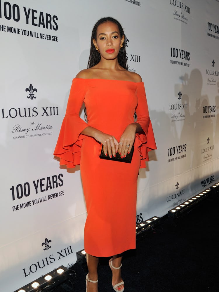 Solange Knowles posing while wearing an orange dress