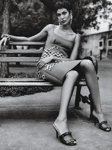 A woman sitting on a bench while wearing a dress and earrings