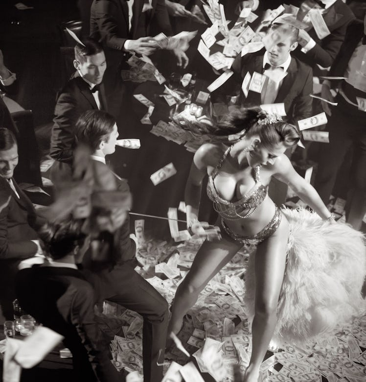 A woman wearing sequined underwear and a feather tail dancing in front of men in suits while they th...