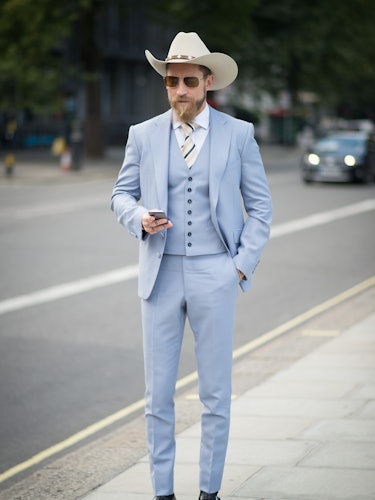 Justin O’Shea wearing a light blue formal suit and a white hat at the 2014 London Fashion Week