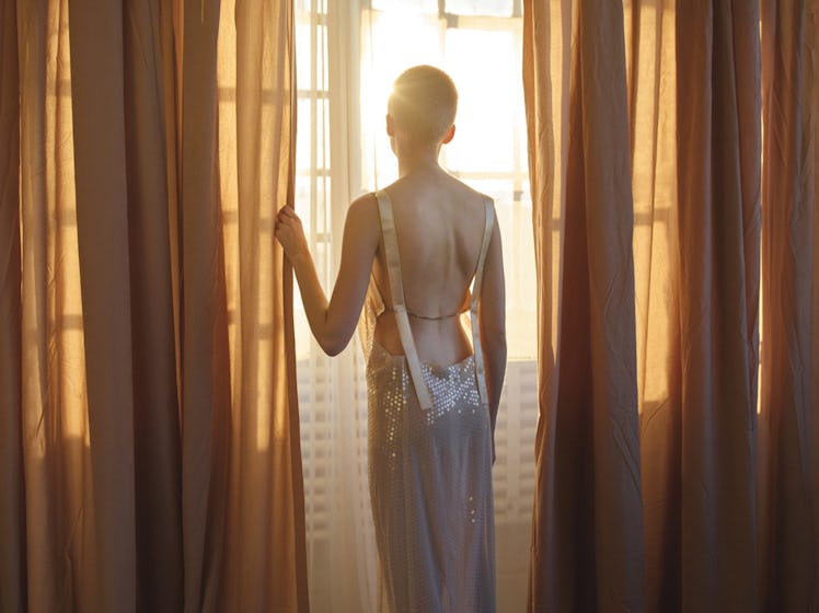 Ruth Bell gazing through the window while wearing a backless long dress