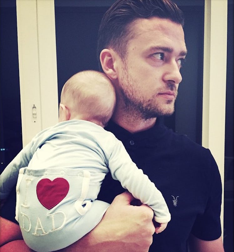 An Instagram post with Justin Timberlake standing in a black shirt while holding his baby in a blue ...