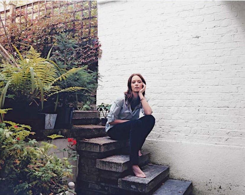 Emily Blunt sitting and posing on stairs in a grey shirt and black trousers