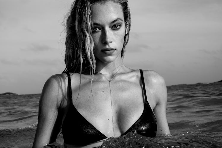 A female model standing in water while wearing a black bikini top