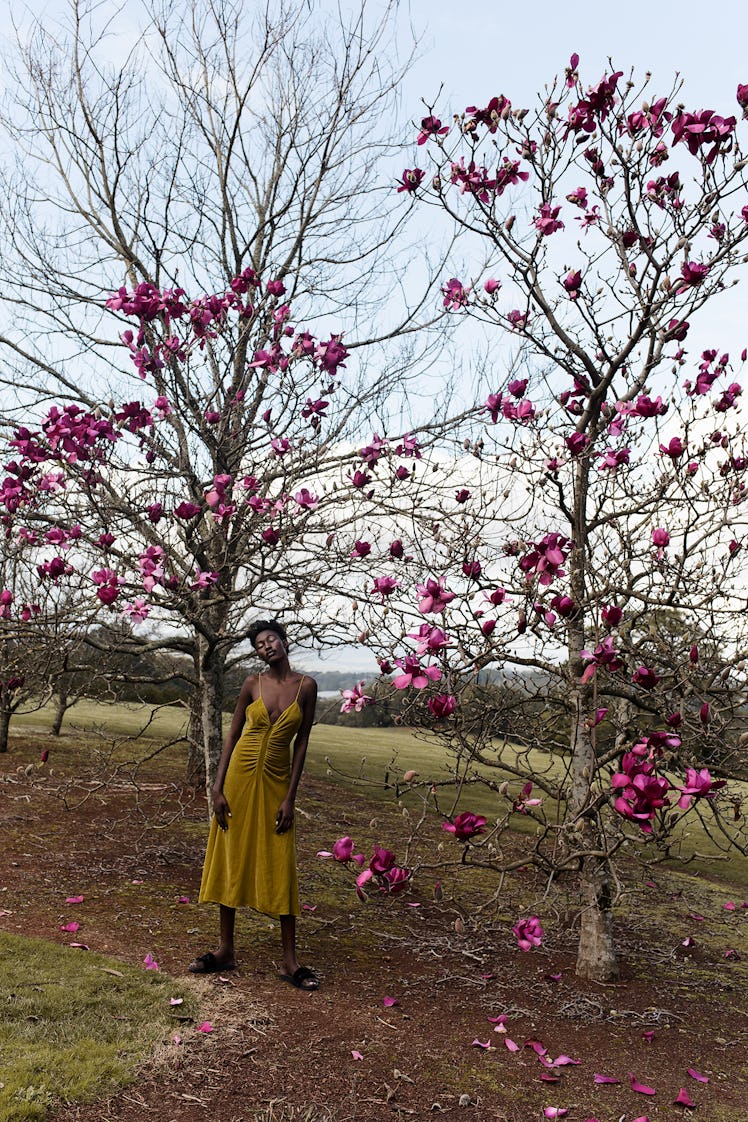 A female model wearing a dark yellow dress while standing under a tree