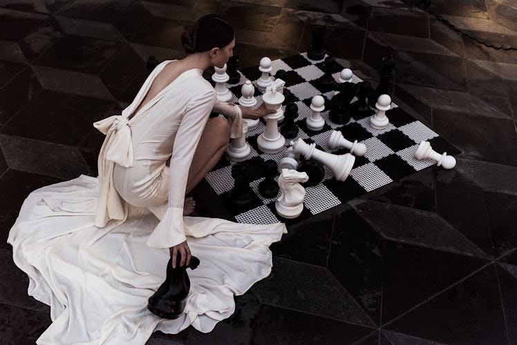 A woman playing chess while wearing a white gown and crouching