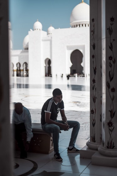 Two men sitting and slouching on a bench with a large white mosque in the background by Dawid Rus