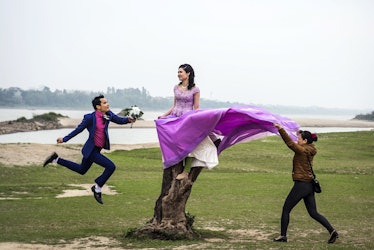A woman in a purple dress posing on a rock, a man holding her dress and another man jumping by Dina ...
