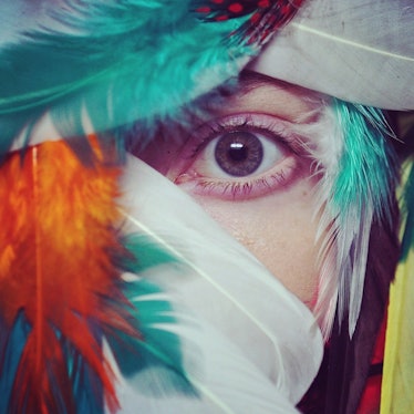 A close-up of a woman's eye surrounded by white, green and orange feathers by Isabel Martinez