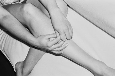 A close-up of a woman's legs while holding her hands over them by Simbarashe Cha