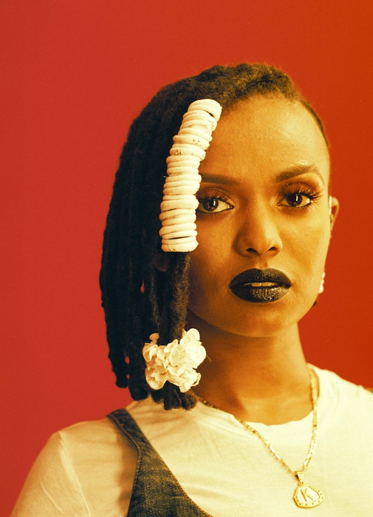 A portrait of a woman in a white shirt with decorated dreadlocks and a red background by Tyra Mitche...