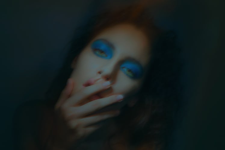 A blurry portrait of a woman with blue eyeshadow covering her mouth with her hand by Vali Barbulescu