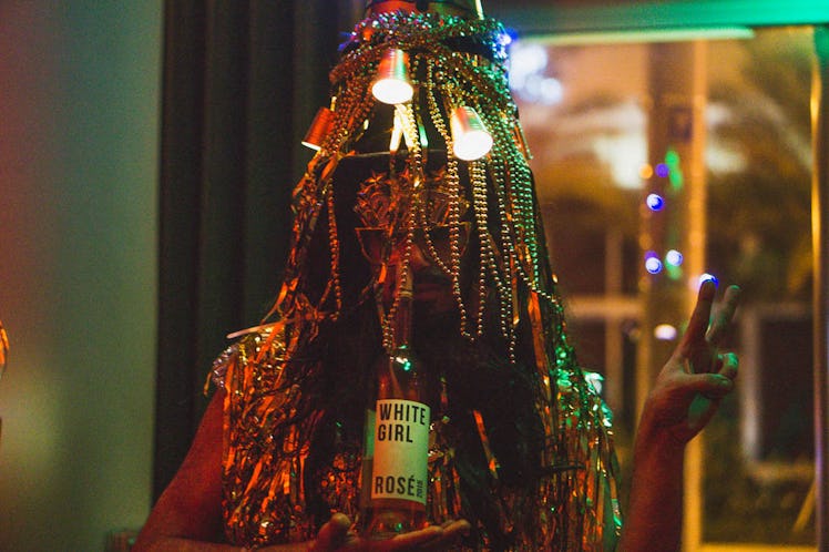 A person with a beaded head piece cover their face, drinking from a bottle at the Make it A Meme-Wor...
