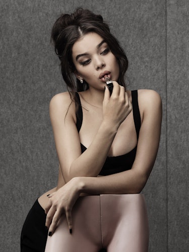 Hailee Steinfeld posing in a black top while putting on lipstick