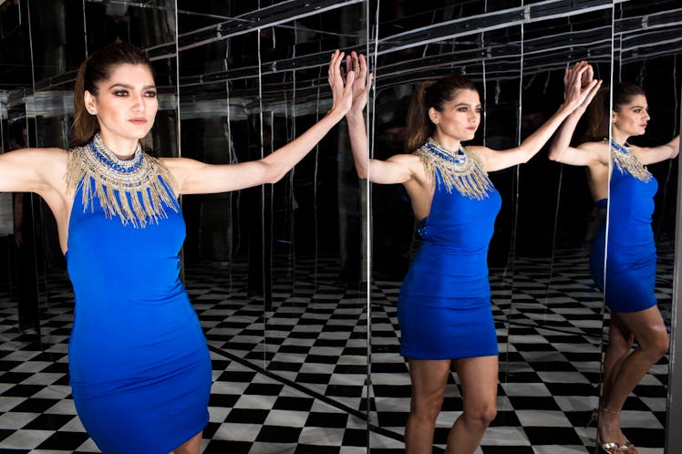 A model in a blue dress with golden detailing around the neck standing between two mirrors at W's pa...