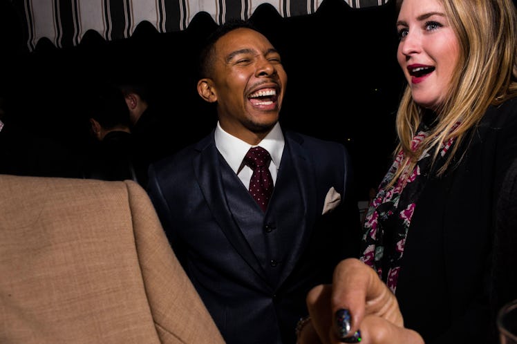 A man in a three-piece grey suit and maroon tie laughing next to a blonde woman at W's Golden Globes...