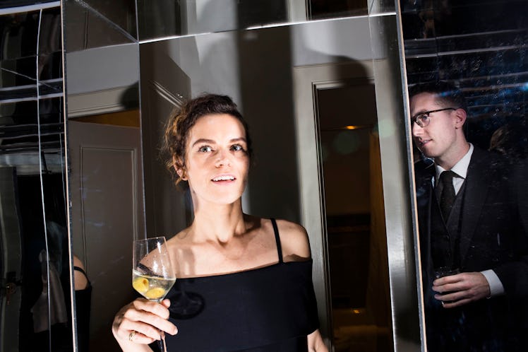 A woman in a black off-the-shoulder dress with straps, holding a glass of white wine at the W party