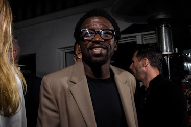 A man wearing glasses, a beige blazer and black shirt smiling at the camera at W's Golden Globes par...