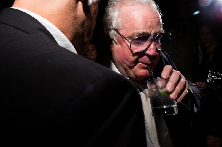A man in glasses, sipping on his drink as he listens to another man telling him something at the W p...