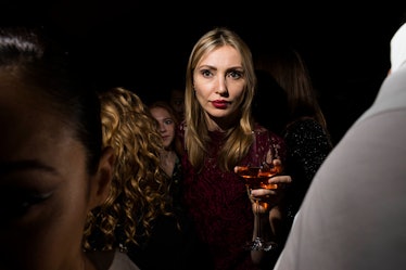 A blonde woman with red lipstick and red dress holding a drink as she walks through the crowd at W's...