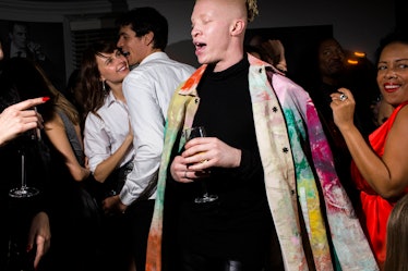 A ma in a multicolored coat and a black sweater dancing with a drink in his hand at W's Golden Globe...