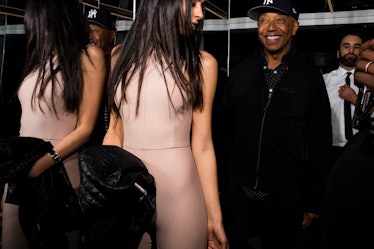 A woman in a skin-tight beige pants and top set, looking behind her at a man wearing a snapback 