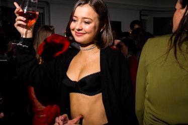 A woman in a black bralette and black jacket dancing with a drink in her hand at W's party