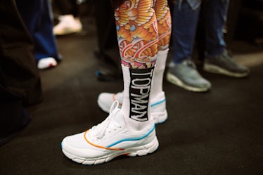 A model standing while wearing orange leggings and white shoes