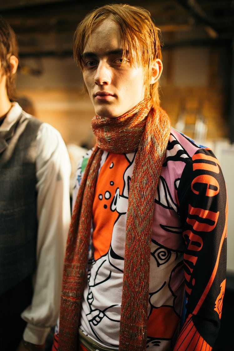 A model posig while wearing an orange scarf and a colorful shirt with long sleeves