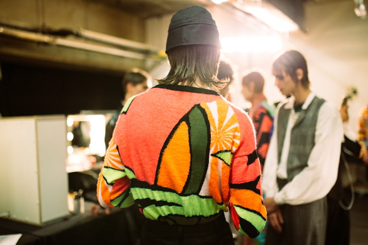 Back of a model that is wearing a black cap and an orange shirt 