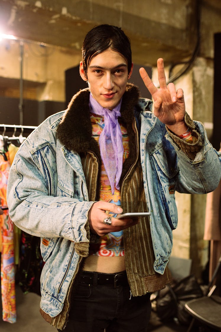 A male model posing in a denim Texas jacket while pointing his index and middle fingers 
