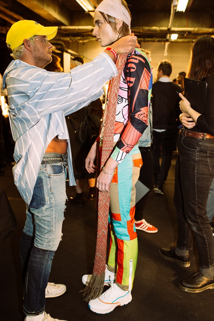 A designer putting an orange scarf around a neck of a model 